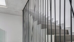 Un escalier moderne avec une rampe en métal, menant à un palier séparé par une cloison en verre.