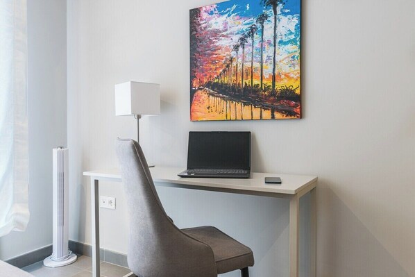 Una habitación moderna con un escritorio, una computadora portátil y un cuadro de un atardecer.