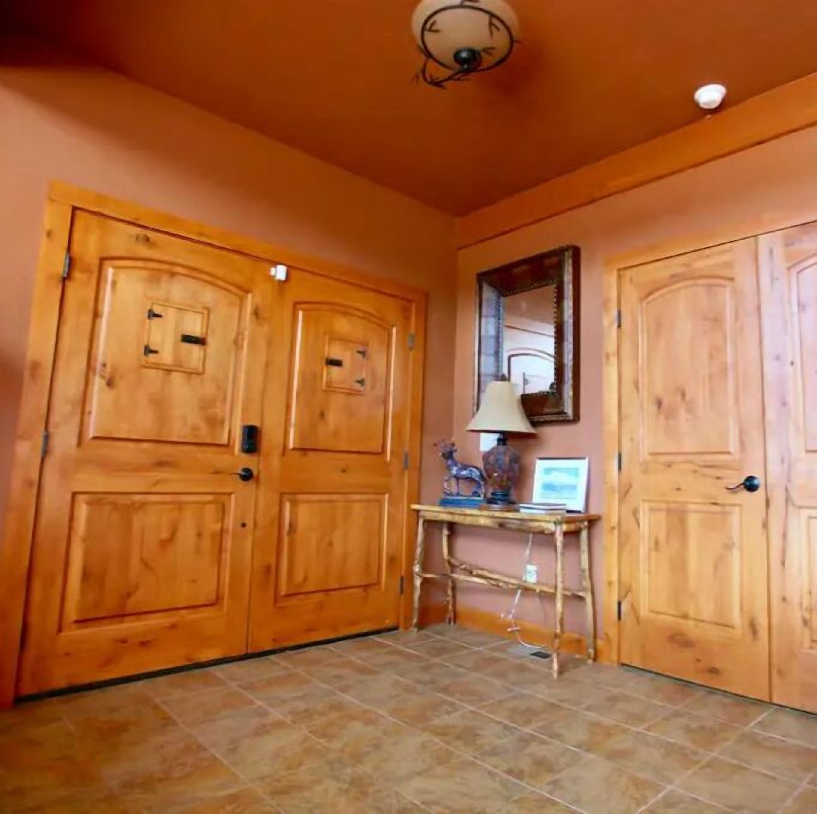 A hallway with wooden doors, a tiled floor, and a small table with a lamp and decorative items.