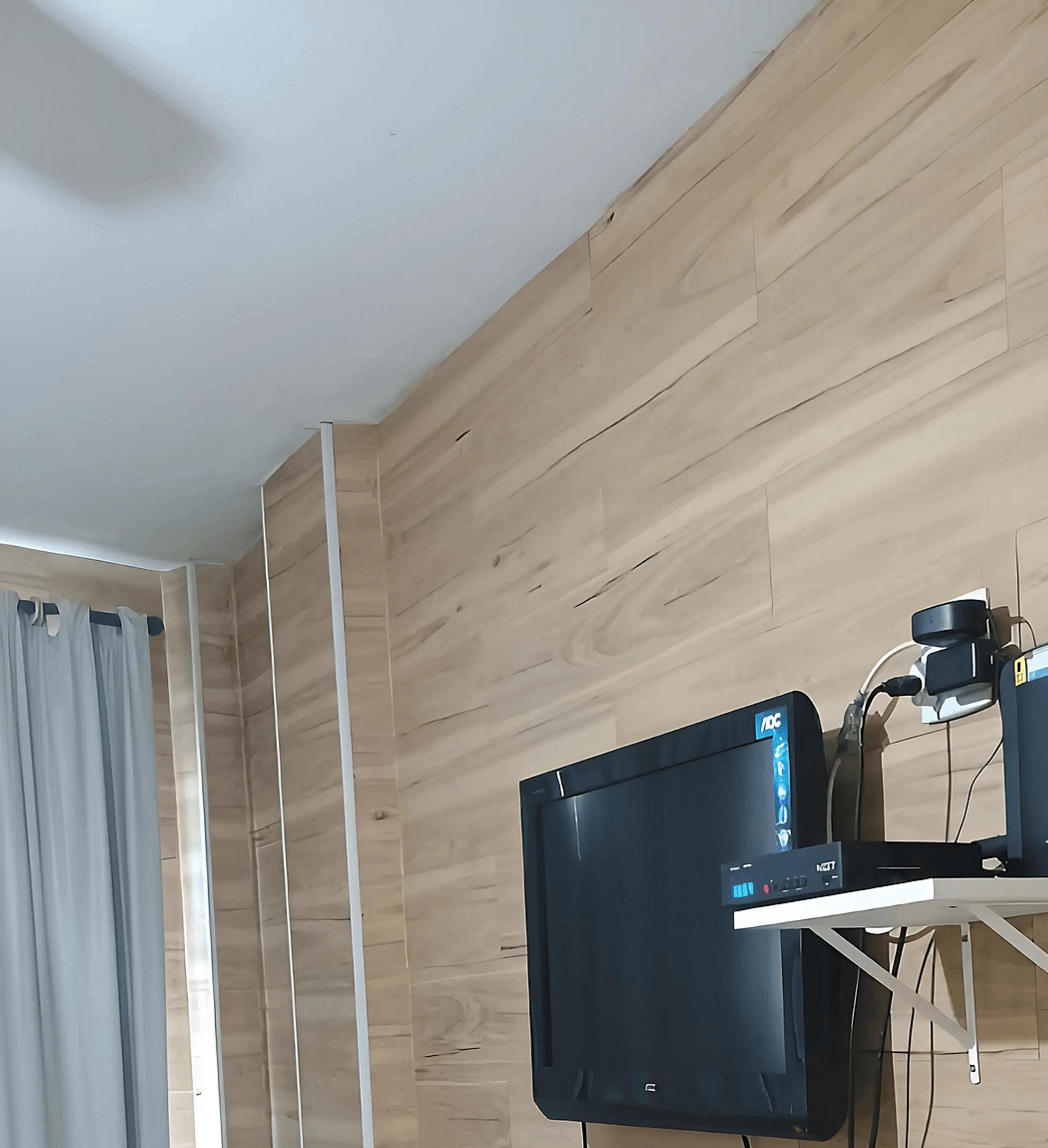 A room with wooden panel walls, a black flat-screen TV mounted on a white stand, and a ceiling fan.