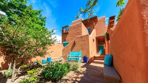 A courtyard with a blue bench, a small tree, and a building with a blue door. - Zona Rosa 75, San Antonio (Santa Fe)