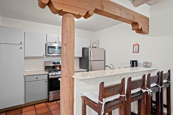 A modern kitchen with white cabinets, stainless steel appliances, a wooden beam ceiling, and a bar area with wooden chairs. - Zona Rosa 75, San Antonio (Santa Fe)