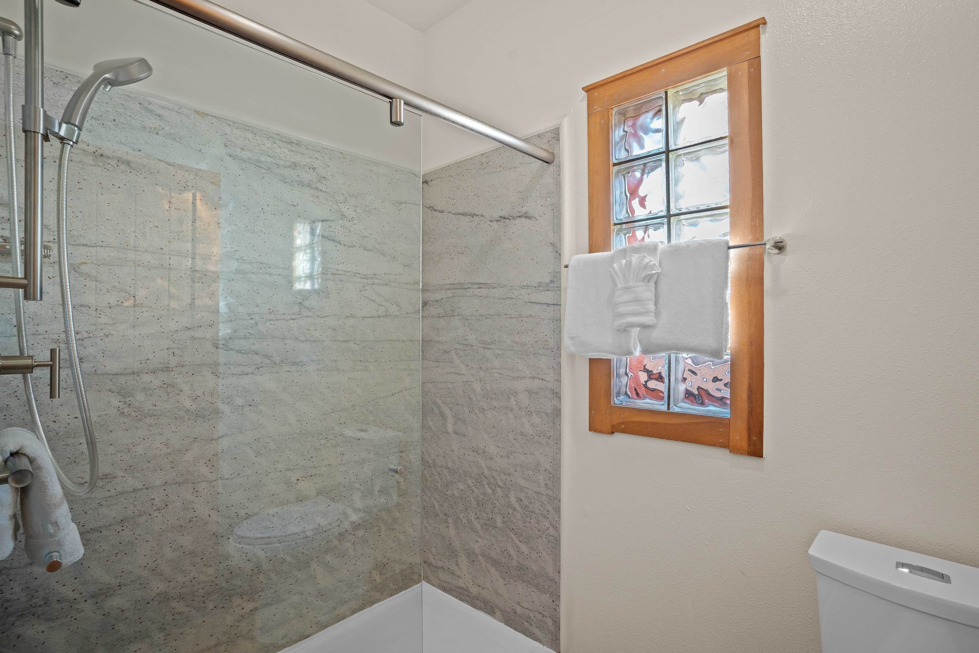 Een badkamer met een douchecabine van glas, een wit toilet en een raam met houten kader.