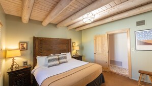 A bedroom with a wooden headboard, a large bed with patterned pillows, a nightstand with a lamp, and a door leading to another room. - Zona Rosa 73, Santa Barbara (Santa Fe)