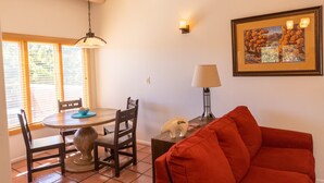 A dining area with a round table, chairs, and a lamp. There is a framed picture on the wall and a red couch in the foreground. - Zona Rosa 73, Santa Barbara (Santa Fe)