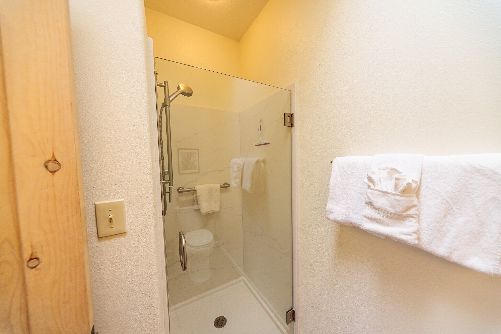 Un bagno con cabina doccia in vetro, un water e un porta asciugamani con un asciugamano bianco.
