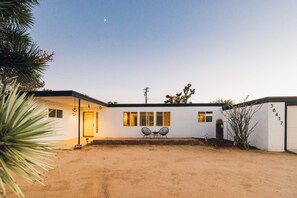 Una casa moderna con fachada blanca, un garaje y un camino de acceso de tierra.