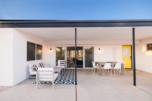 Un patio cubierto con una mesa y sillas de comedor, un sofá y un tapete estampado.