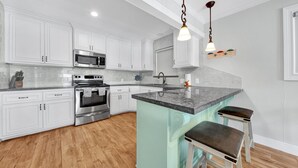 A kitchen with white cabinets, stainless steel appliances, a granite countertop, and a hanging light fixture. - Lugo Fishing Paradise in Historic Port Isabel (Port Isabel)