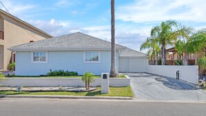 A single-story residential house with a grey roof, white exterior walls, and a small front yard with a palm tree and shrubs. - Lugo Fishing Paradise in Historic Port Isabel (Port Isabel)