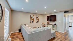 A modern living room with a grey sofa, wooden flooring, and a flat-screen TV mounted on the wall. - Quiet, Cozy Townhouse w/ all new appliances and furniture. (Shreveport)