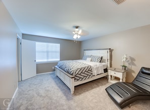 A bedroom with a bed, nightstand, chair, and a window with blinds.