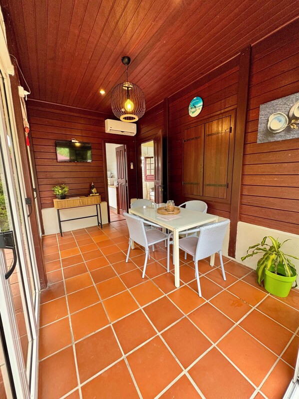 A covered patio with a tiled floor, a table with chairs, a hanging light fixture, and a green potted plant.