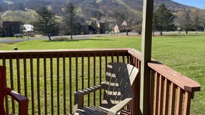 Una terraza de madera con una sola silla Adirondack, con vistas a un campo de césped y una carretera con edificios al fondo.