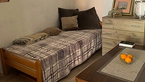 Et lille, hyggeligt værelse med en enkeltseng, et trænatbord, et lille bord med appelsiner og et kommode med et spejl og billeder i rammer.