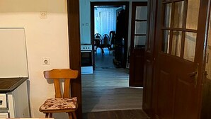 En smal gang med en trædør, der fører til et spiseområde med et bord og stole.