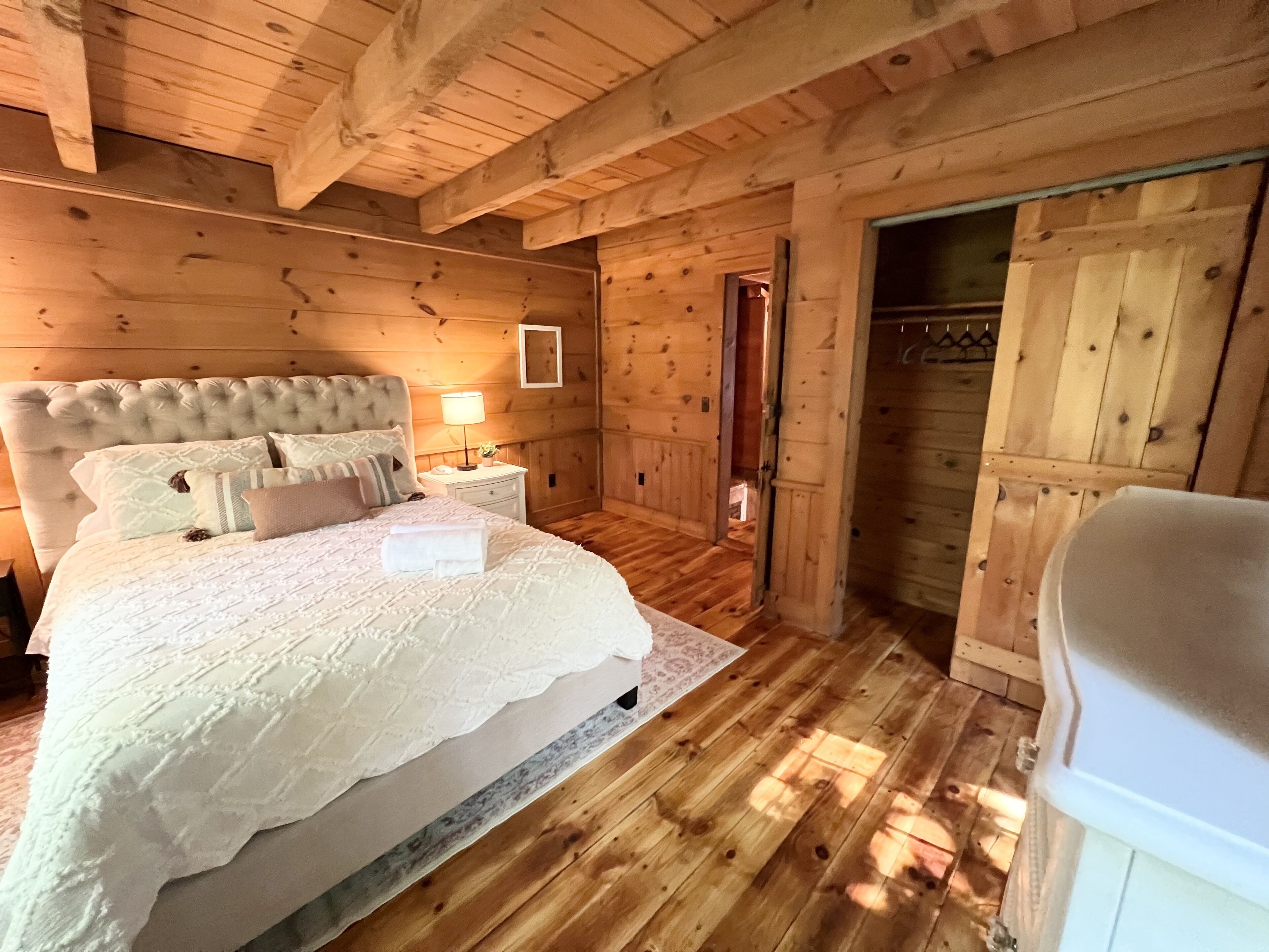 Un dormitorio de cabaña de madera con una cama grande, una mesita de noche, una lámpara y un armario.