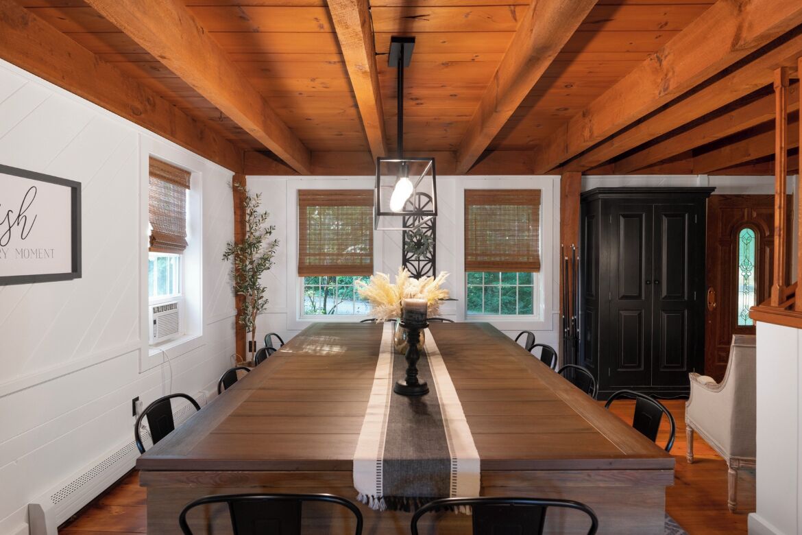 A dining area with a long wooden table, black chairs, a central candle holder, and a hanging light fixture.