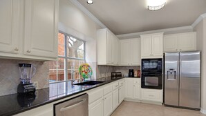 A modern kitchen with white cabinets, stainless steel appliances, a black countertop, and a window with a view of a brick wall.