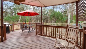 A wooden deck with a red umbrella, a grill, and a rocking chair.