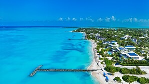 Un resort costero con un muelle que se adentra en aguas turquesas, rodeado de exuberante vegetación y edificios modernos.