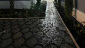 Una casa con un sendero empedrado que conduce a la entrada, una antena parabólica en el techo y un pequeño jardín con plantas y un árbol.