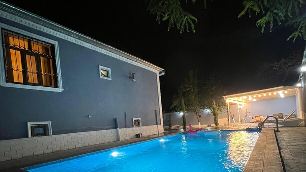 Una piscina junto a un edificio con una ventana que muestra cortinas anaranjadas.