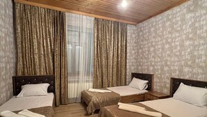 Una habitación de hotel con dos camas individuales, piso de madera, un ventilador de techo y una ventana con cortinas.