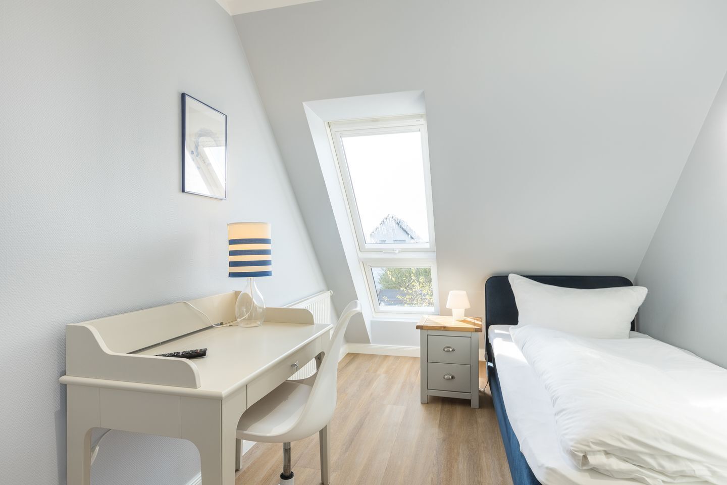 A bedroom with a bed, a desk, a chair, a nightstand, and a window.