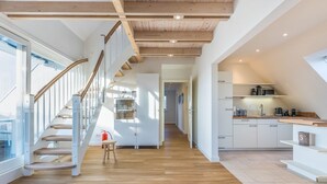 A modern interior with a wooden staircase, a kitchen area, and a view through a glass door. - Appartement Friesenloft (Sylt-Ost)