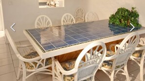Un espace repas avec une table carrelée, des chaises blanches et un luminaire suspendu.
