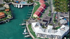 Une vue aérienne d’une marina où sont amarrés de nombreux bateaux, d’un grand bâtiment doté d’un toit blanc et d’une série de constructions aux toits rouges qui bordent le rivage.