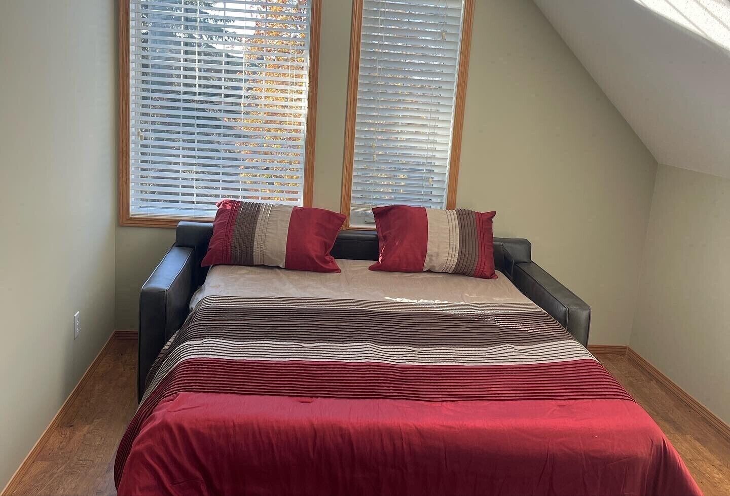 A bedroom with a bed, two windows with blinds, and a sloped ceiling.