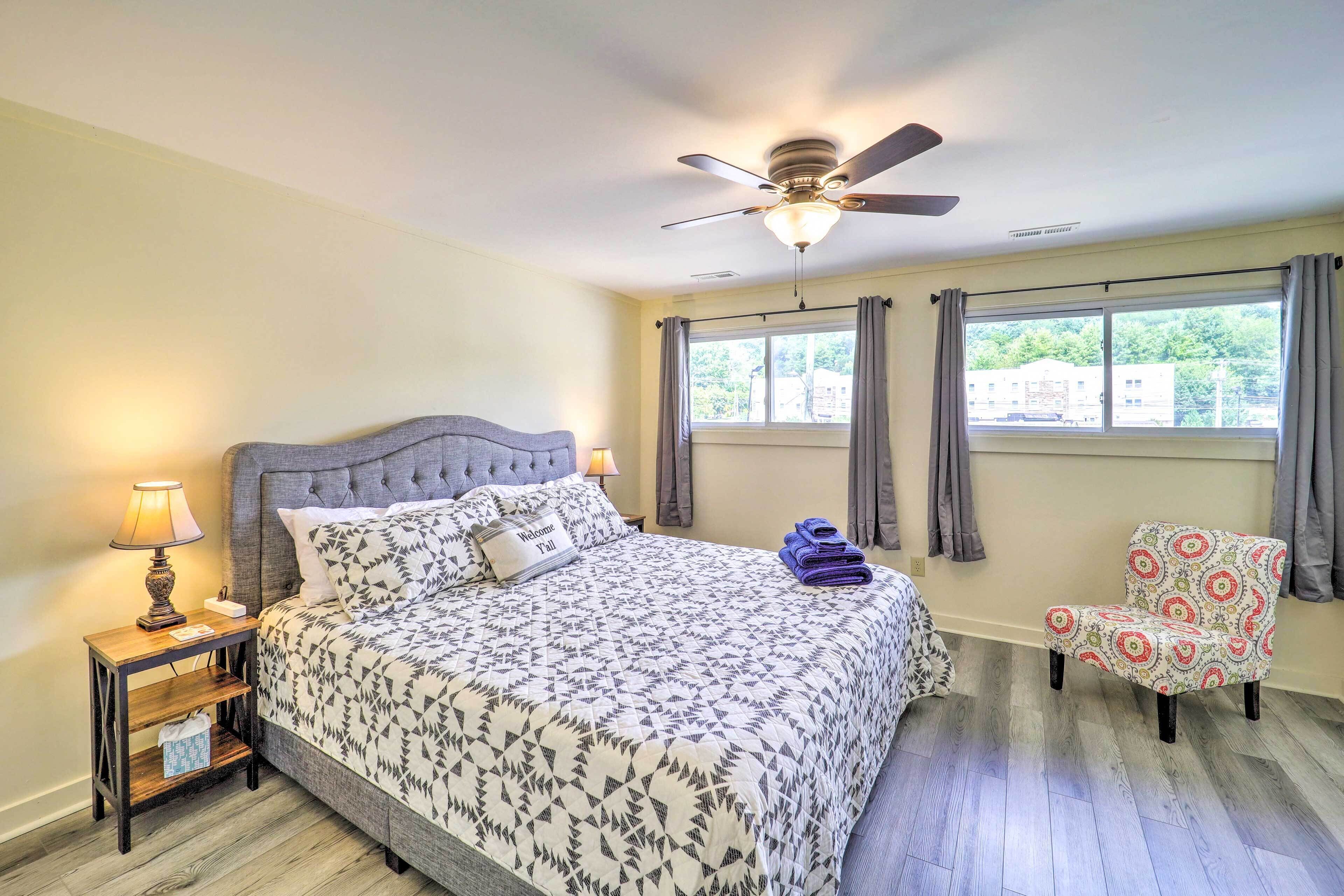 A bedroom with a bed, a nightstand with a lamp, a chair, and a ceiling fan.