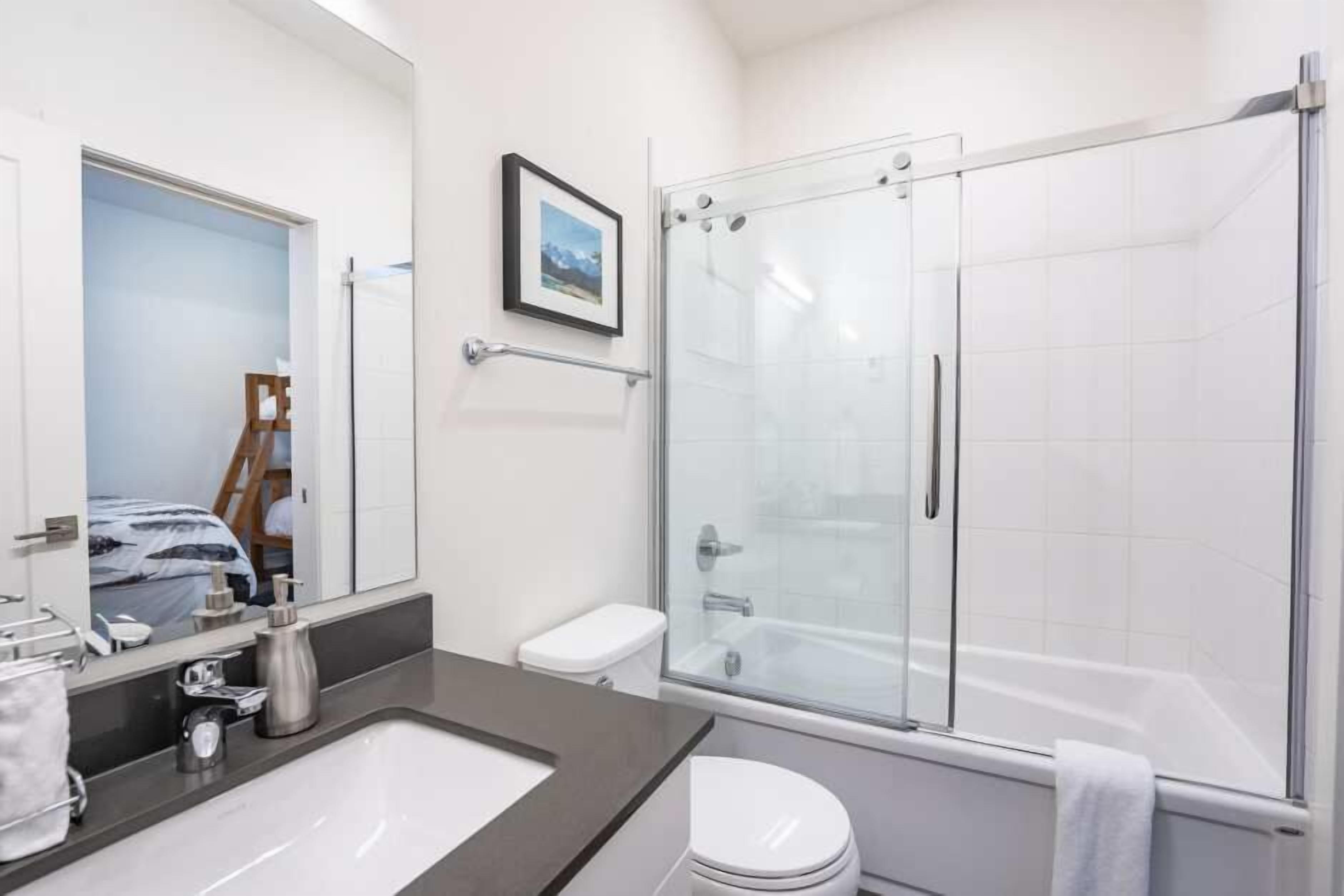 A modern bathroom with a glass-enclosed shower, a white toilet, and a large mirror.