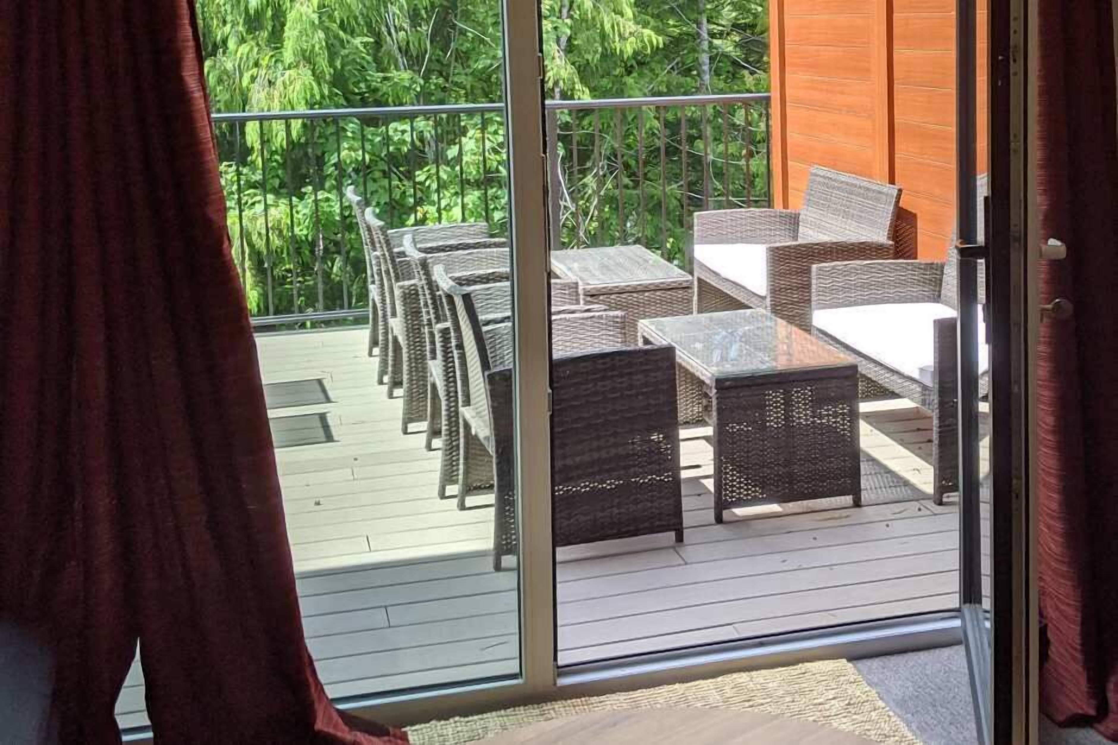 A balcony with wicker furniture and a glass door leading to a lush green area.