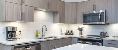 Una cocina moderna con armarios grises, un lavavajillas de acero inoxidable, un microondas integrado y una encimera blanca.