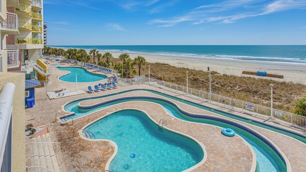 A pool area with multiple swimming pools, lounge chairs, and a view of the beach. - Updated North Myrtle Beach Condo w/ Lazy River! (North Myrtle Beach)