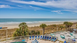 A beach view with a pool area, lounge chairs, and tables. - Updated North Myrtle Beach Condo w/ Lazy River! (North Myrtle Beach)