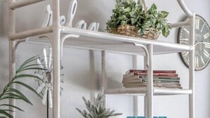 Una estantería metálica blanca con diversos objetos decorativos y plantas.