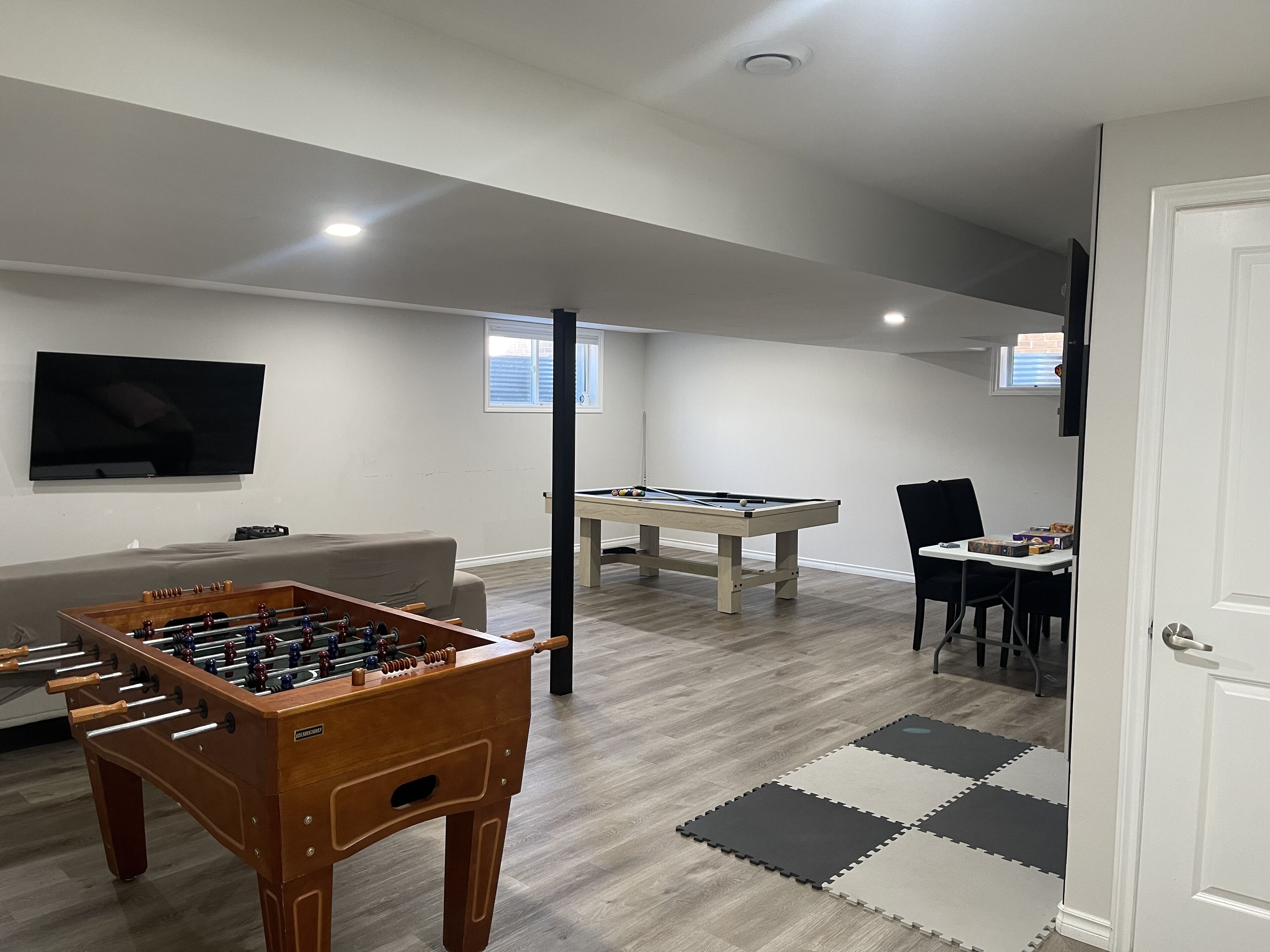 A living room with a foosball table, pool table, and a TV mounted on the wall.