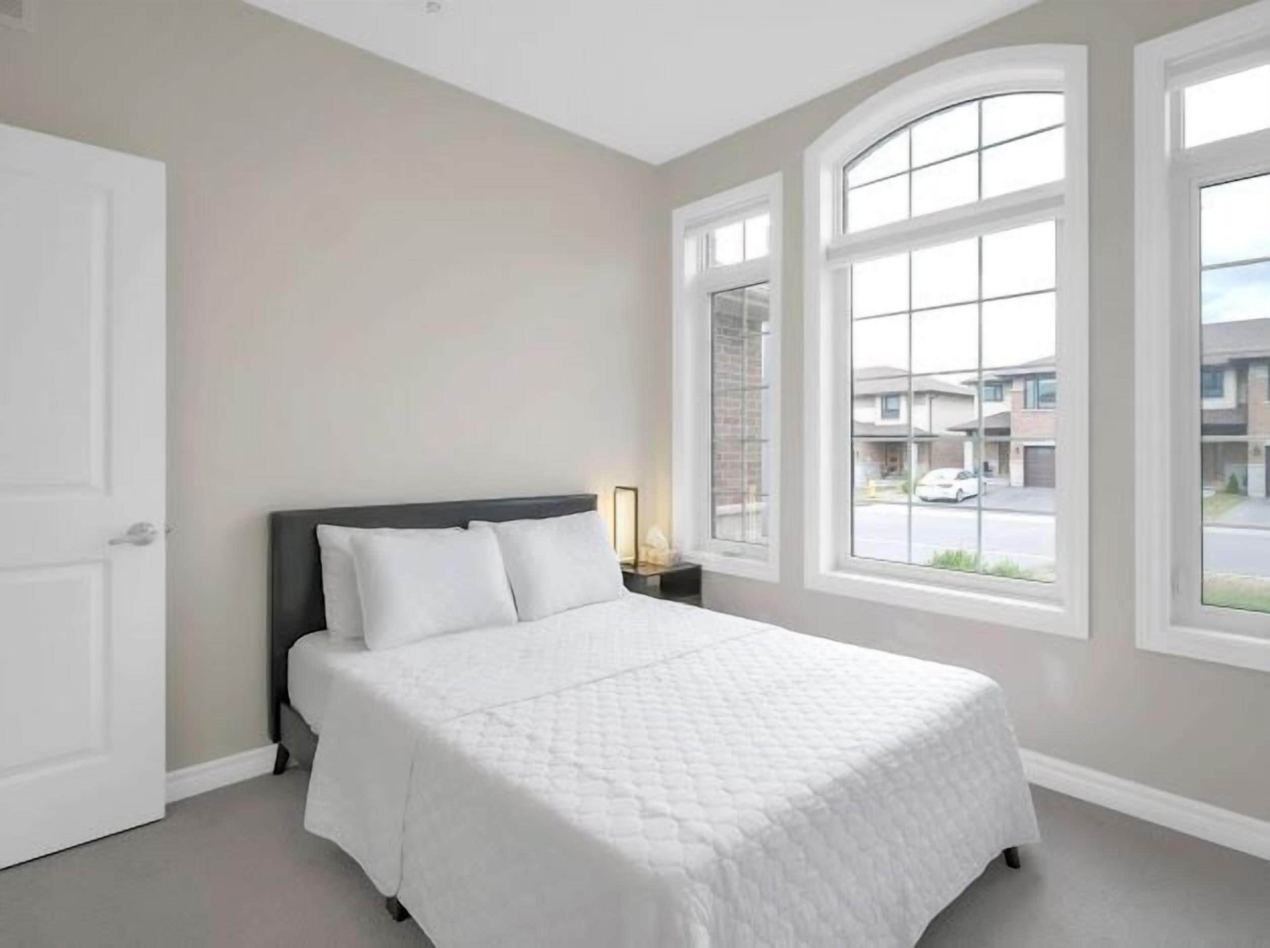 Un dormitorio con cama, mesita de noche y ventanas amplias.