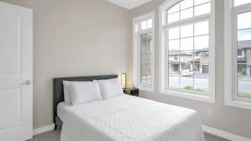 Un dormitorio con cama, mesita de noche y ventanas amplias.