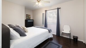 A bedroom with a bed, a ceiling fan, a chair, a window with blinds, and a trash bin. - Enjoy a Peaceful Get-Away - Self check -in (San Antonio)