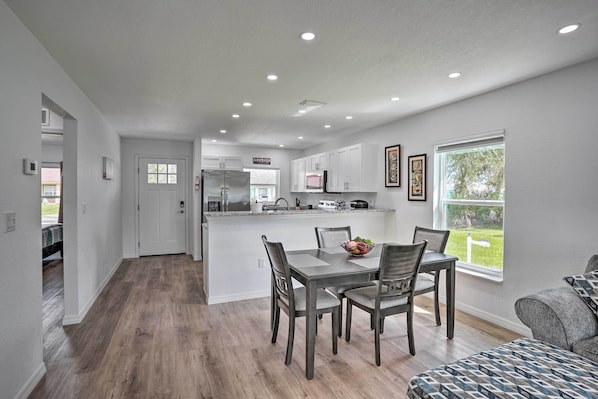 A modern kitchen with white cabinets, a central island, and a dining area with four chairs.
