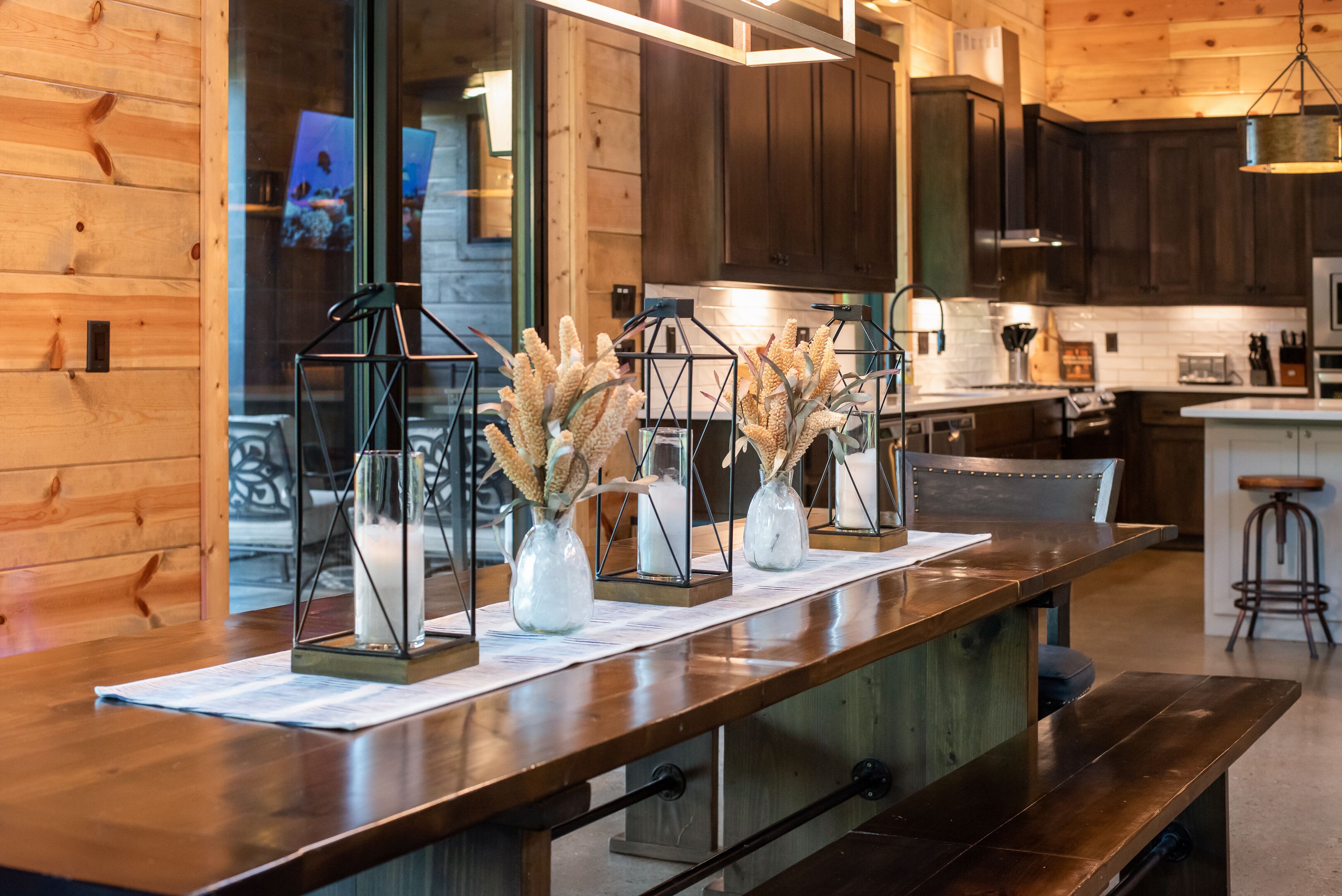 A wooden interior with a long counter, three glass vases with dried plants, and dark wooden cabinets.