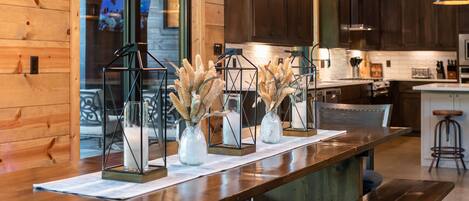 A wooden interior with a long counter, three glass vases with dried plants, and dark wooden cabinets.