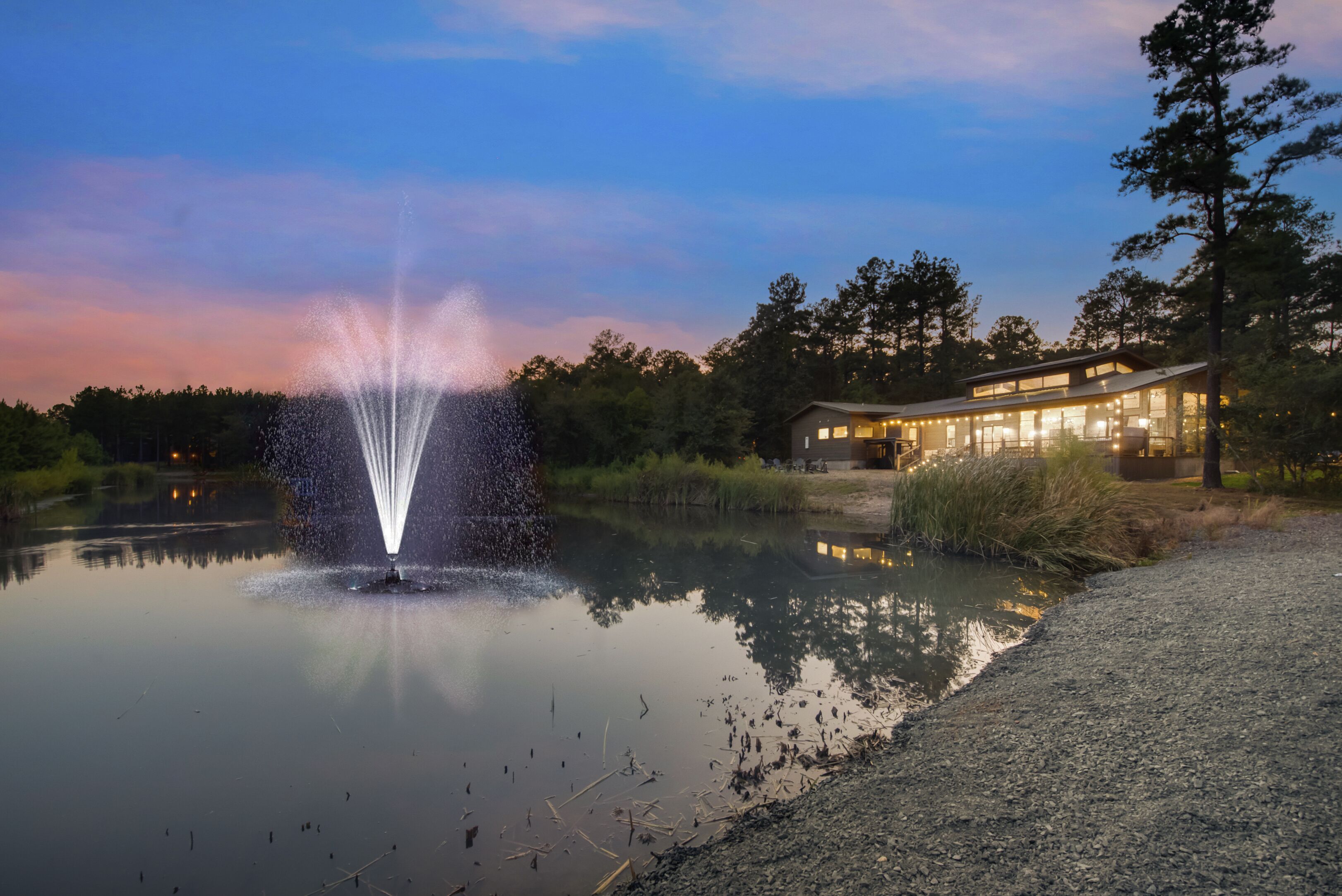 A tranquil lakeside setting with a fountain, a modern building with large windows, and a clear sky.