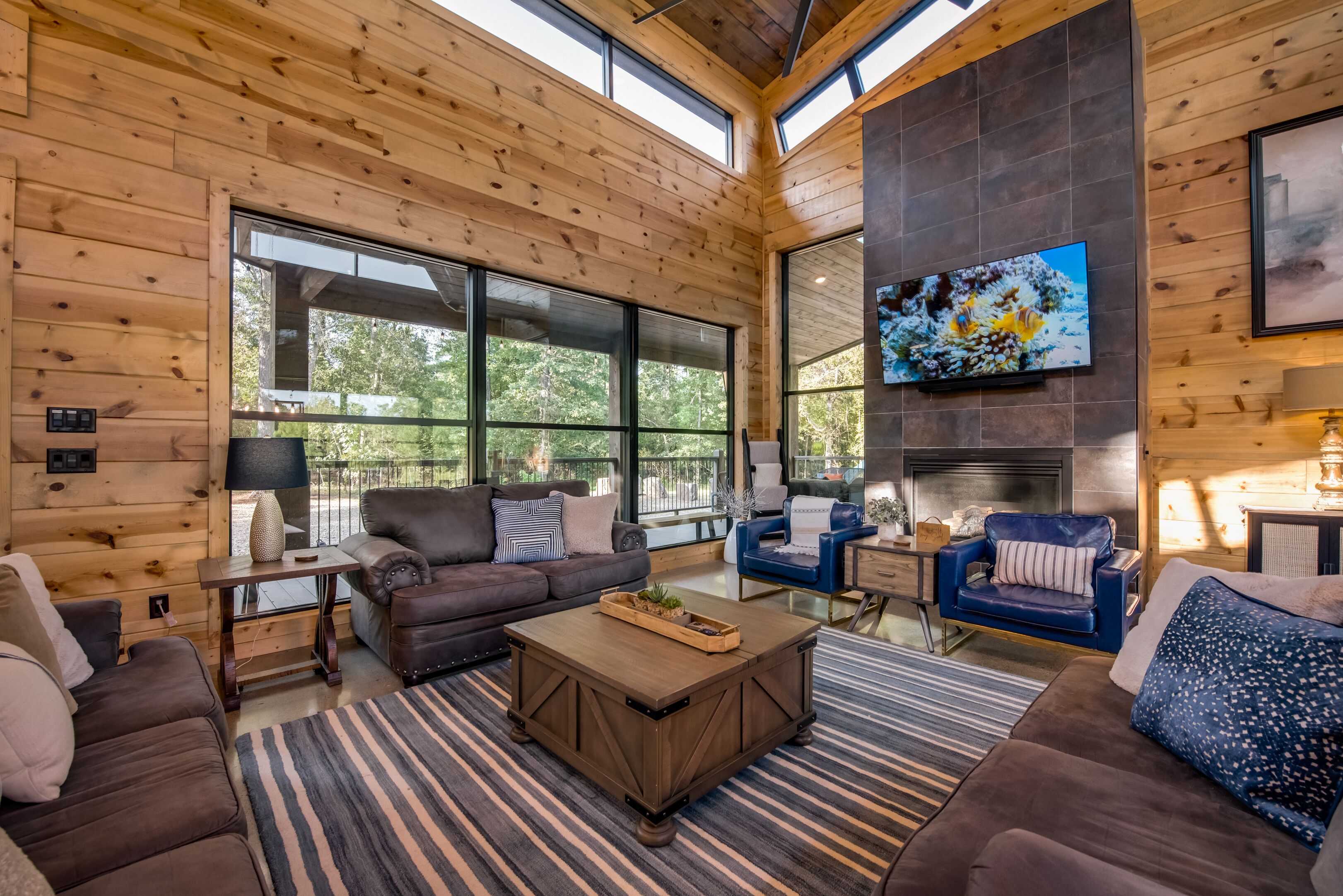 A spacious living room with a large fireplace, wooden walls, and large windows.
