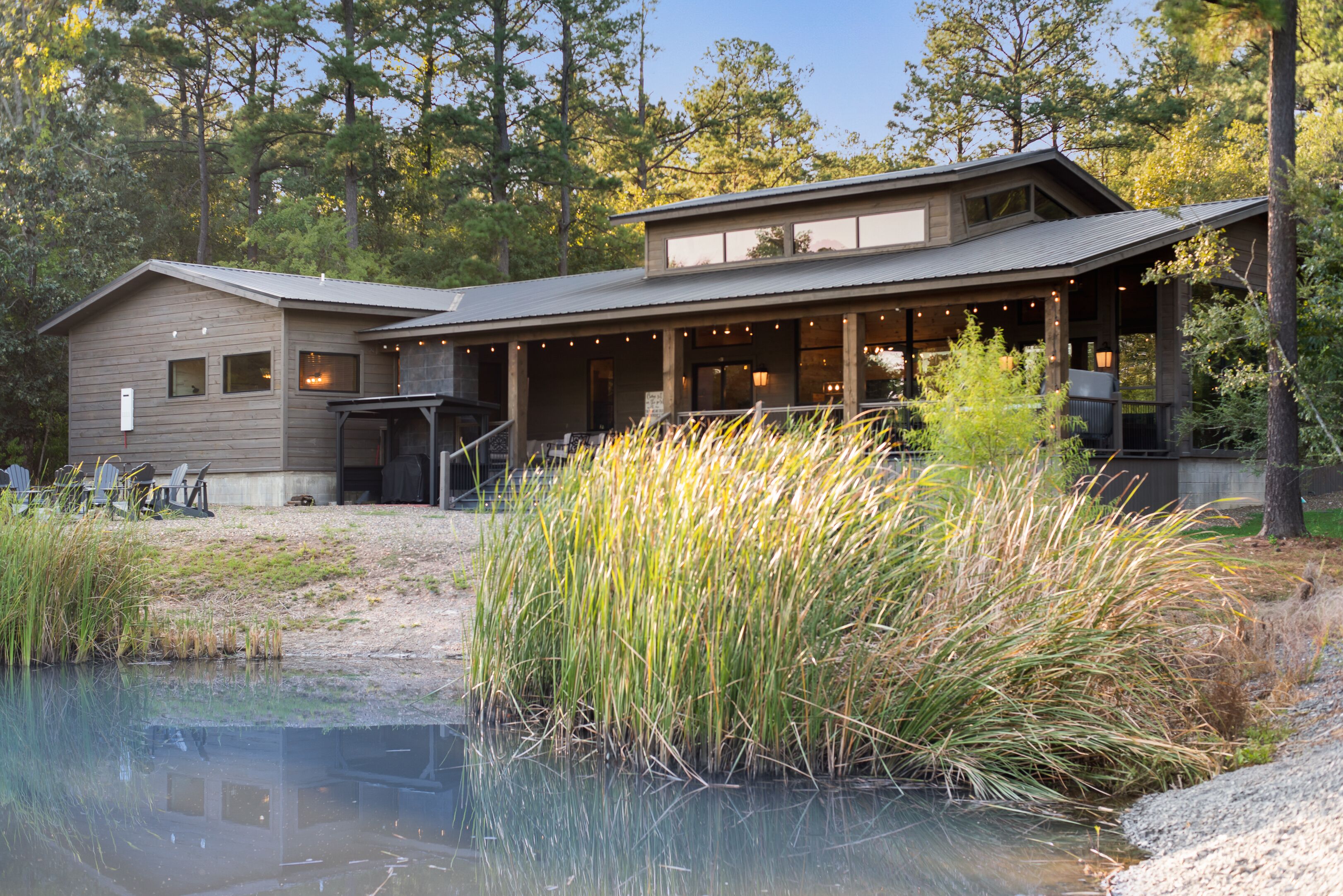 A lodge with a covered patio, a pond, and surrounding tall grasses.